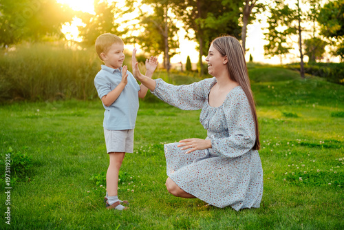 mom and child playing on a green lawn in the park in the summer, having fun together, mother and small child walking in the summer, playing on the grass