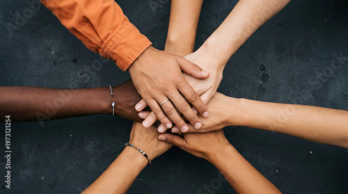 Diverse group of people stacking hands in a circle, showing unity and teamwork on a dark background.