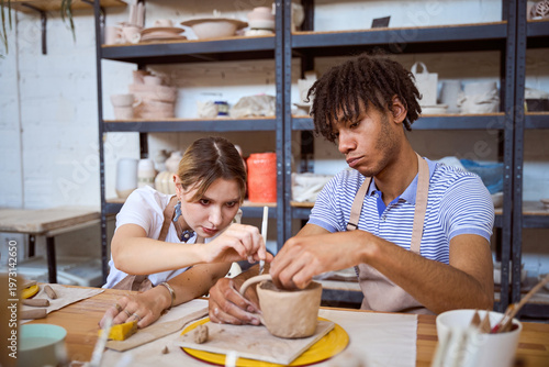 Young adults working with clay on pottery wheel in studio