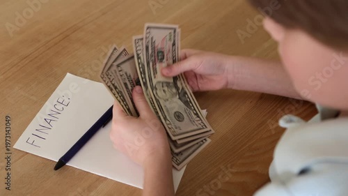 Wealthy kid holding large fan of dollar bills next to finance note, rich child with lots of cash, money and wealth concept, financial success indoors close-up