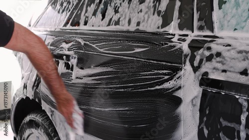 Man hand scrubbing soapy foam on dark car with sponge, manual car washing and detailing close-up, vehicle cleaning service, auto care maintenance