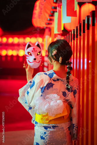 Fotografie Rear view of a woman in yukata holding a fox mask standing in front of red lanterns at Fushimi Inari Taisha at night