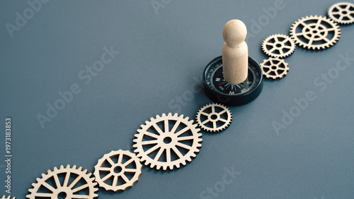Wooden figure standing on a compass amidst gears representing a leader guiding a team toward a specific goal or direction.