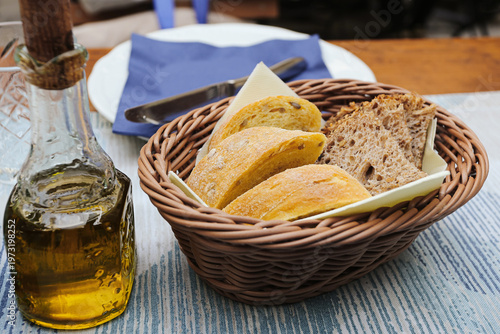 Basket with fresh bread slices served on table with olive oil bottle. Rustic food setting in restaurant. Simple meal concept with bakery products and natural ingredients.