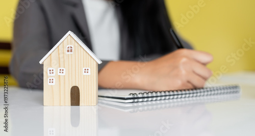 Quadro su tela Small house model on table with blurred woman writing in notebook