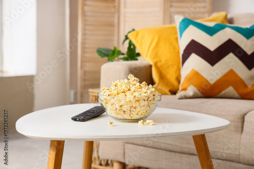Tasty popcorn with TV remote controller on table in living room