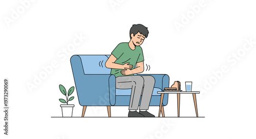 A distressed young man wearing a green t-shirt sits on a comfortable blue armchair while clutching his painful stomach near a small wooden side table.