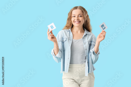 Young woman holding papers with vitamin B on blue background