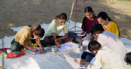 Indian villager girl boy sitting on mat do study read book outdoor rural area ground place. Happy group child hold notes talk gossip enjoy desi life new day outside open class field
