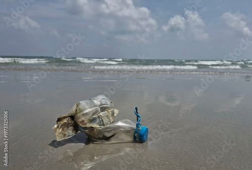 Environmental Imperil: A discarded plastic bottle and cap lie abandoned on a serene beach, highlighting the impact of plastic pollution on pristine shores, under a serene sky.