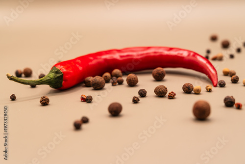 Vibrant red chili pepper rests among scattered peppercorns on a neutral background