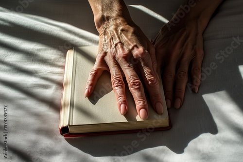  Close-up of hands with detailed skin and nails resting on open book in warm sunlight.