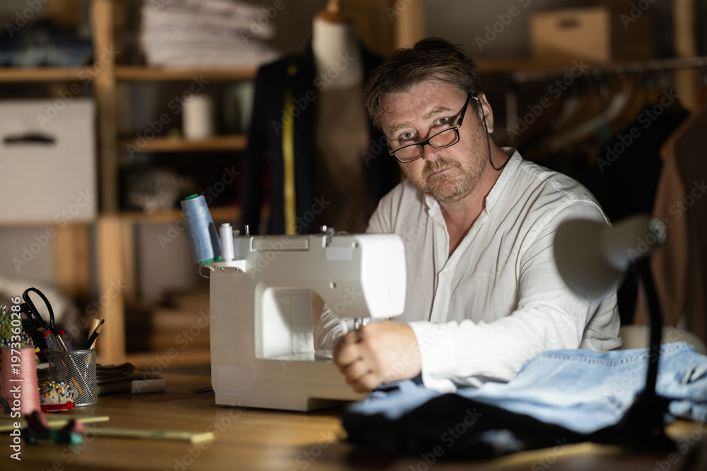 Fototapeta premium Middle-aged male dressmaker working with sewing-machine at night