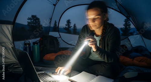 Woman using laptop inside tent at night, focused on work with a flashlight beam illuminating the keyboard, enjoying remote work in nature