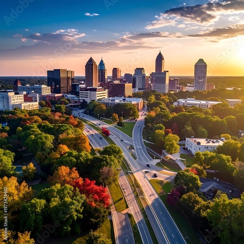 An aerial view of a cityscape with modern skyscrapers amidst lush trees, a highway, and a warm sunset