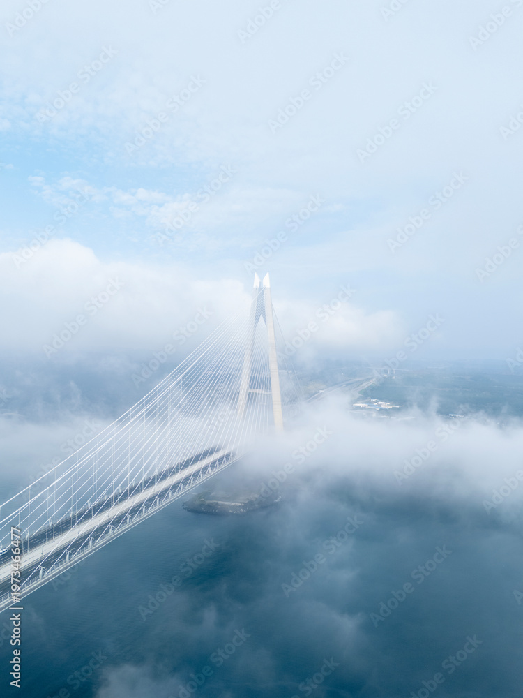 Fototapeta premium Vertical aerial view of Yavuz Sultan Selim Bridge pylon rising through a thick sea of white clouds in Istanbul. Ethereal and misty Bosphorus landscape at Poyrazkoy. Modern engineering in the sky. Atmo