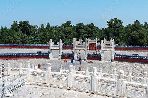 A peaceful view of the Temple of Heaven grounds in Beijing, featuring elegant white stone railings, traditional gates, and lush green trees under a clear blue sky. Beijing, China, 27 May 2025