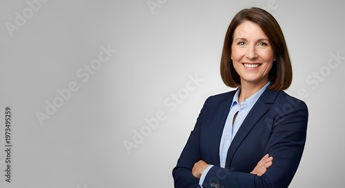 Confident corporate professional woman with a warm smile, posing in a navy blazer and light blue shirt against a neutral gray background, conveying trust and leadership.