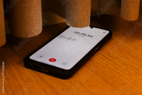 Voice detection and recording app in mobile phone listening to conversation placed on the floor near window curtains. Secretly grabbing and wiretapping inside home or apartment during covert operation