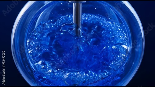 Vibrant blue liquid stirring vigorously in a clear glass container close-up.