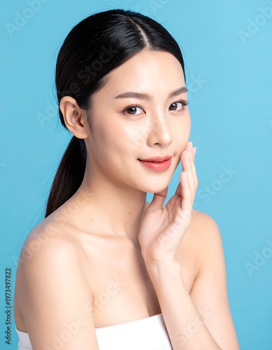 A radiant young woman with dark hair pulled back, posed with her hand near her face, against a blue backdrop