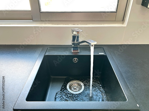 Kitchen black sink, faucet with running water. Saving resources, utility bills. Water resources, water cost