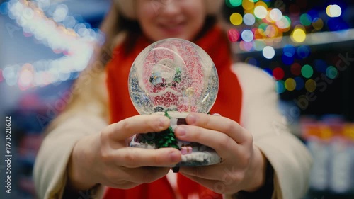 A close-up of a Christmas snow globe with Santa in a woman's hands