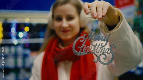 A woman holding a Merry Christmas ornament in a festive holiday store