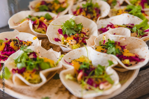 Delicious mini fish tacos served as appetizers, featuring vibrant red cabbage, fresh mango salsa, black sesame seeds, and cilantro garnish on small soft tortillas at a professional catering event.