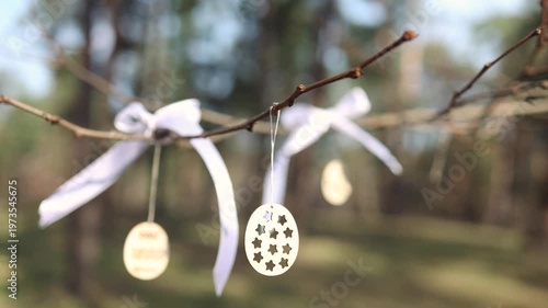 Beautiful spring sunny nature background. Handmade wooden Easter egg decor hanging on branches outdoor. New green buds symbol of early spring season, Palm sunday, Easter. 