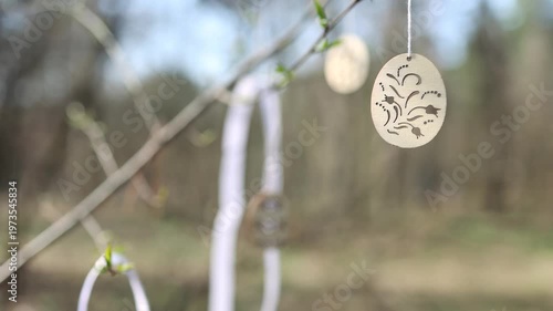 Beautiful spring sunny nature background. Handmade wooden Easter egg decor hanging on branches outdoor. New green buds symbol of early spring season, Palm sunday, Easter. 