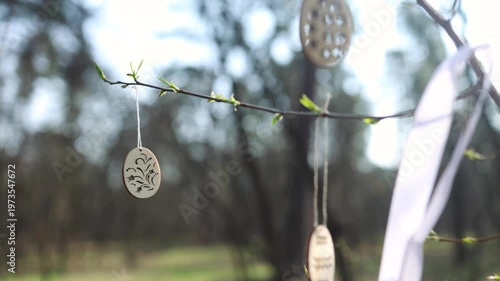 Beautiful spring sunny nature background. Handmade wooden Easter egg decor hanging on branches outdoor. New green buds symbol of early spring season, Palm sunday, Easter. 
