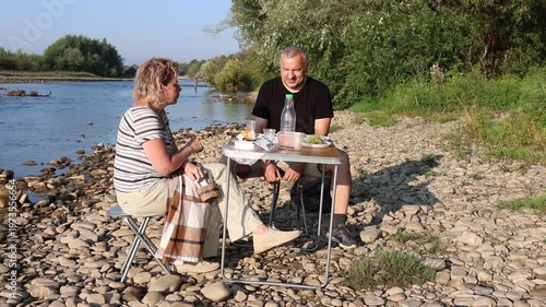 A man and woman had a picnic on the riverbank, enjoying food and drinks.