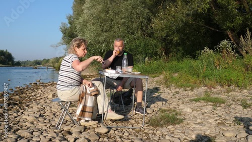 A man and a woman sit with their backs to the camera on a riverbank, relaxing and spending time outdoors