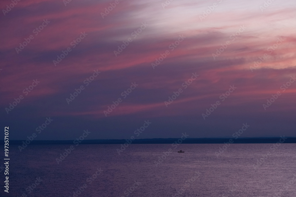 Obraz premium A minimalist seascape at twilight featuring a vast purple and pink sunset sky over calm water with a tiny boat on the horizon. 