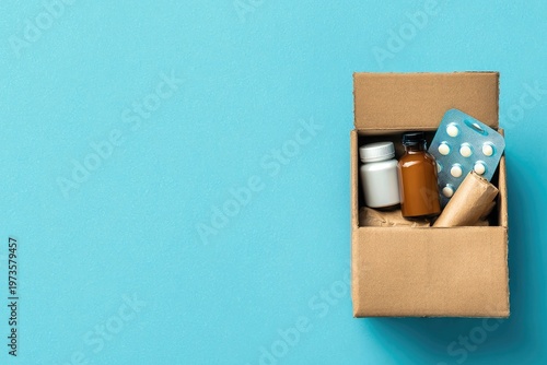 Cardboard Box Filled with Medications and Medical Supplies on Blue Background.