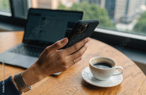 Close-up of a businesswoman using a smartphone while working remotely at a modern desk with laptop and coffee, natural light, lifestyle scene.