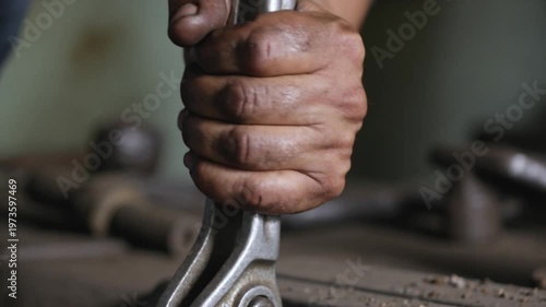 Close-up of a skilled artisan's dirty hand holding a wrench, working in a workshop.