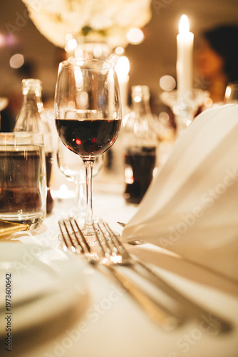 Close-up of a wine glass with red wine on a set dinner table with candles and elegant bokeh background. Perfect for wedding celebrations, romantic fine dining, luxury events, and festive banquets.