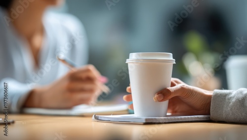 Close-up of a person holding a disposable coffee cup during a meeting.