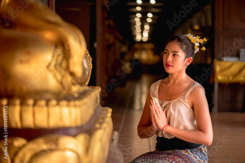 Fotografie Thai woman in traditional Northern Thai drress sitting in front of Buddha image