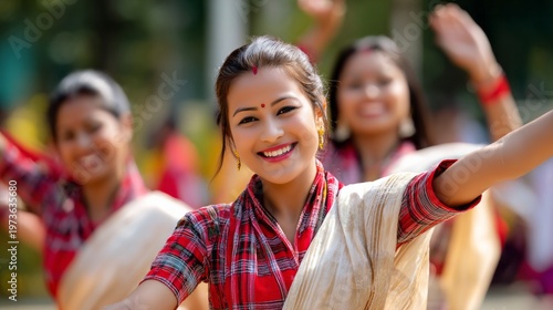 Joyful young woman with bindi and traditional attire dancing, celebrating bohag bihu. Blurred women dancing in background