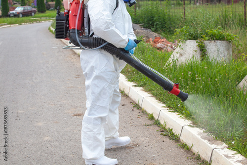 Billede på lærred Pest control worker spraying herbicide on overgrown roadside grass in protective