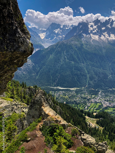 Expansive view from from La Flégére a mountain ridge revealing the Chamonix valley with a town nestled below and the snow-capped mont blanc mountain range dominating the dramatic alpine landscape.