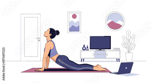 Young woman practicing cobra yoga pose on a mat in living room while following an online fitness tutorial on her laptop computer.