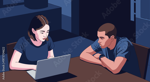 Two people using a laptop computer together at a table in a dimly lit room, focusing on digital collaboration