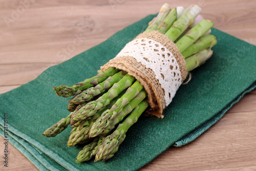Photos Frischer grüner Spargel im Jutebund mit Spitzenborte auf einem grünen Küchentuch