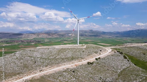 Footage of wind farm, a renewable energy source, green farmland and a cloudy blue sky.