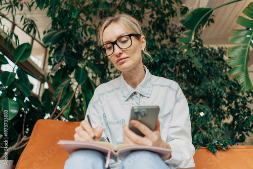 Φωτογραφία Middle aged business woman sitting on couch and writing note in copybook in a modern office