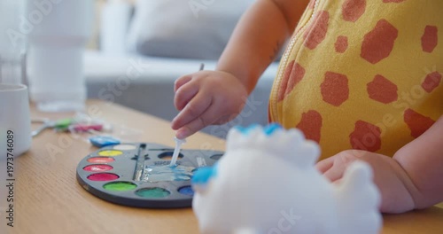 Young toddler uses a water dropper on a colorful paint palette at a home table, focusing on early childhood education, fine motor skill development, and creative indoor playtime.